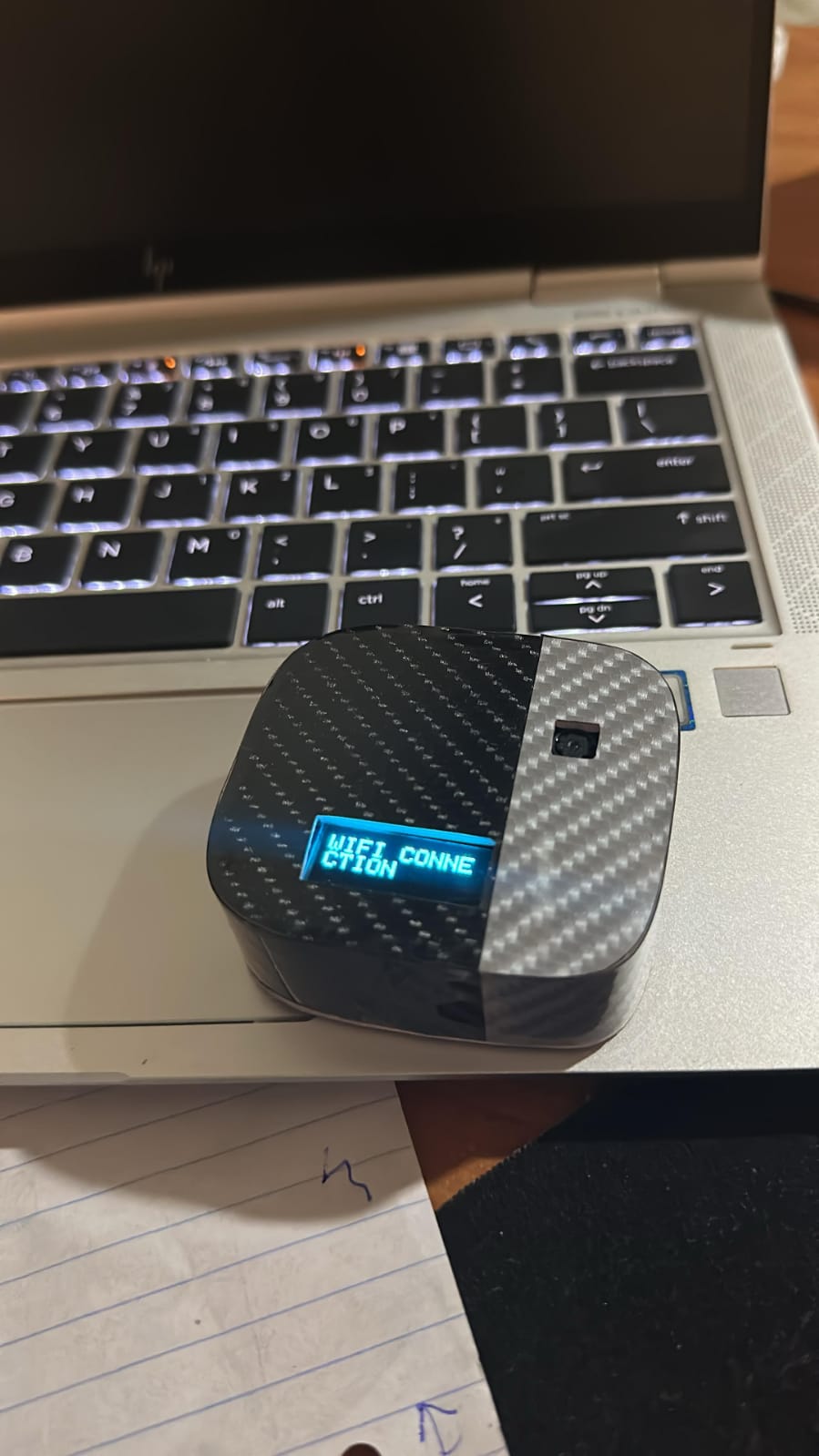 Carbon-fibre wrapped device with an OLED screen showing a WiFi status